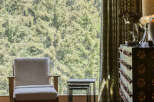 Experience rustic charm with this cozy armchair positioned by a large window overlooking a lush forest.