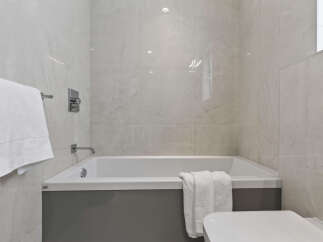 Experience modern luxury in this bathroom featuring a sleek bathtub with a grey base and pristine white tiling.
