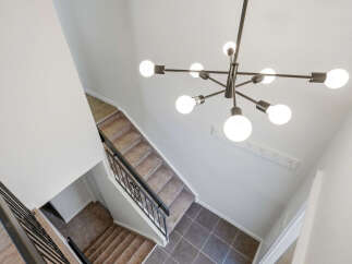 Ascend to the upper level via a carpeted staircase, featuring a modern black railing and a striking Sputnik chandelier overhead.