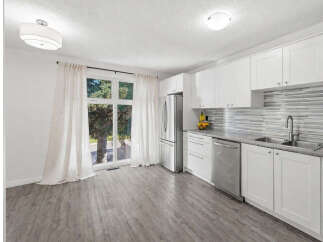 This modern kitchen features sleek white cabinetry and a stylish mosaic tile backsplash, complemented by durable grey laminate flooring.