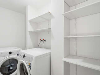 Discover the convenience of this dedicated laundry space, featuring two modern washing machines and ample shelving for storage.