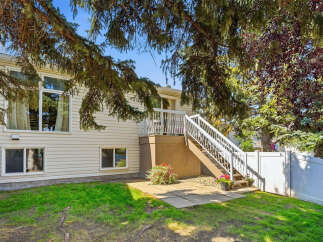 Discover this charming home featuring a spacious backyard with a white vinyl fence and mature trees offering ample shade.