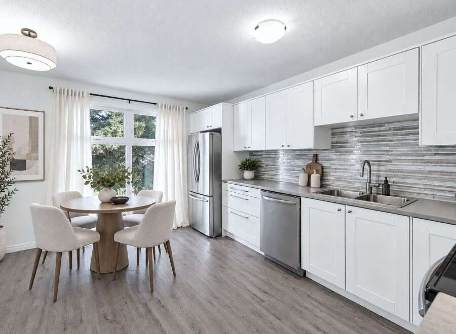 This modern kitchen and dining area features crisp white cabinetry, a sleek mosaic tile backsplash, and stainless steel appliances.