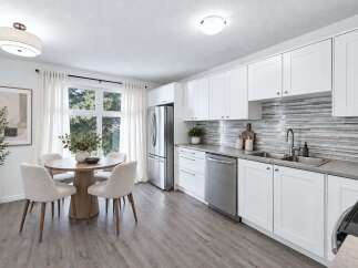 This modern kitchen and dining area features crisp white cabinetry, a sleek mosaic tile backsplash, and stainless steel appliances.