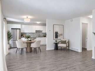 Discover modern living in this open-concept space featuring a sleek white kitchen with stainless steel appliances and a stylish dining area perfect for intimate gatherings.