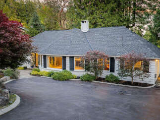 Discover this charming white home nestled amongst mature trees, featuring a welcoming asphalt driveway and a beautifully landscaped yard.