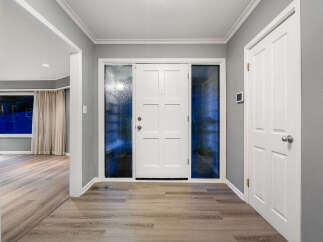 Step into a welcoming entryway featuring a bright white front door flanked by frosted glass windows, offering privacy and natural light.