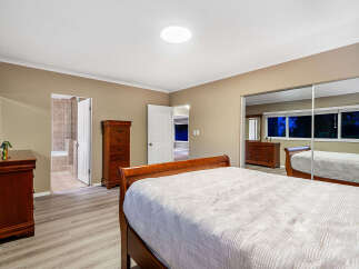 This spacious bedroom features a comfortable king-size bed with a quilted white comforter, complemented by a rich wooden dresser and a matching chest of drawers.