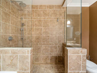 Experience luxury in this spacious bathroom featuring a walk-in shower with elegant travertine tile and a modern chrome shower system.