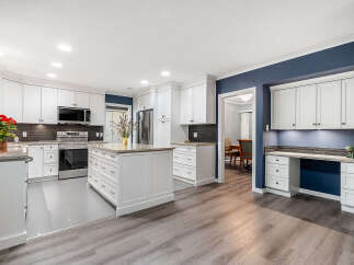 This spacious kitchen boasts modern white cabinetry, a large island with ample storage, and sleek granite countertops.