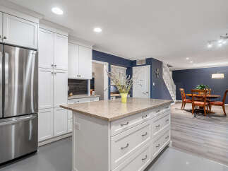 This spacious kitchen boasts modern white cabinetry and a large island with granite countertops, perfect for meal preparation and casual dining.