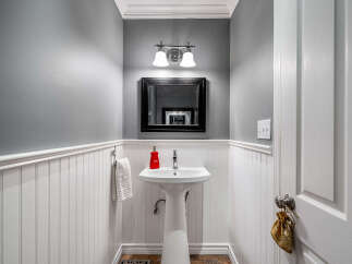 This powder room features a stylish pedestal sink with a chrome faucet and a red soap dispenser, complemented by a large black framed mirror above.