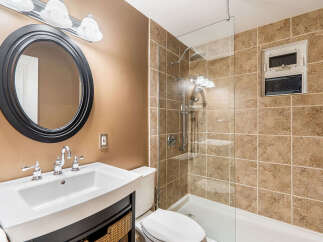 This modern bathroom features a sleek vanity with a white basin sink and chrome fixtures, complemented by a large, round black-framed mirror.