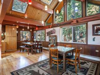 Experience rustic charm in this spacious dining area, featuring a vaulted wood-beamed ceiling with skylights and large windows offering serene forest views.