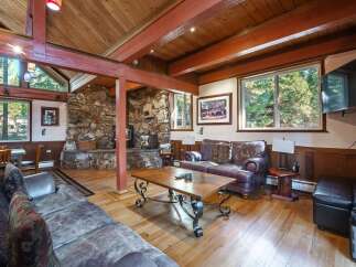 Experience rustic charm in this spacious living area, featuring a grand stone fireplace and exposed wooden beams that create a warm, inviting atmosphere.