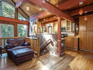 Experience rustic charm in this cozy living space featuring a plush leather armchair and ottoman, perfect for relaxing by the large windows overlooking a serene forest.