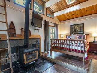 Cozy cabin bedroom featuring a rustic wood-burning stove and a raised platform bed.
