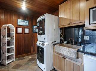 This laundry room boasts a stacked washer and dryer for space efficiency, complemented by a unique granite sink and copper fixtures.