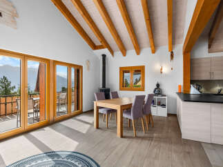 Experience breathtaking mountain views from this charming dining area, featuring a wooden dining table and chairs bathed in natural light from expansive glass doors.