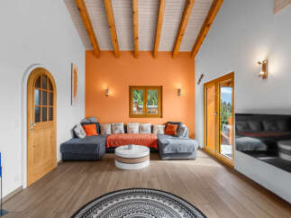 Experience modern alpine living in this stunning living room, featuring a vibrant orange accent wall and exposed wooden beams on the vaulted ceiling.