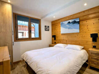 Experience cozy mountain living in this charming bedroom featuring a plush white duvet and a striking ski-themed artwork above the wooden headboard.