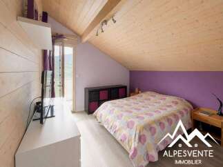 Discover this charming bedroom featuring a cozy bed with a colorful duvet and a wooden ceiling that adds warmth and character.