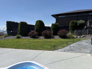 Enjoy outdoor living at its finest with this beautifully landscaped backyard, featuring a lush green lawn, mature trees, and a charming stone pathway.