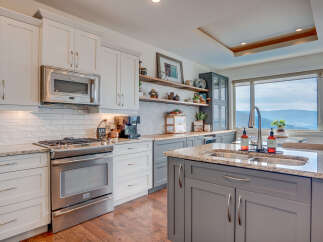Experience breathtaking mountain views from this stunning kitchen, featuring sleek white cabinetry, a modern stainless steel range, and a spacious granite island with a double sink.