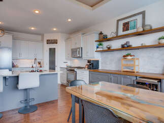 Experience modern living in this stunning kitchen, featuring sleek grey cabinetry, a spacious island with bar seating, and a beautiful wood and resin dining table.
