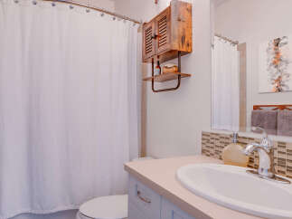 This charming bathroom features a white herringbone shower curtain, a rustic wooden medicine cabinet with a shelf, and a modern vanity with a beige countertop and a sleek chrome faucet.