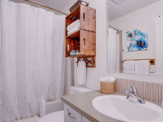 This bright and airy bathroom features a textured white chevron shower curtain, a rustic wooden crate shelving unit, and a modern vanity with a sleek faucet.