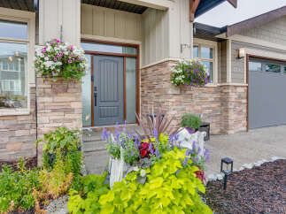Welcome guests with vibrant curb appeal, featuring a stylish gray front door framed by natural stone accents and lush hanging flower baskets.