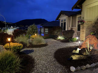 Experience the charm of this beautifully lit home at dusk, featuring a meticulously landscaped garden with decorative lighting and unique garden art.