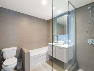 This modern bathroom features a sleek white vanity with a vessel sink, complemented by a glass-enclosed shower with a rainfall showerhead.