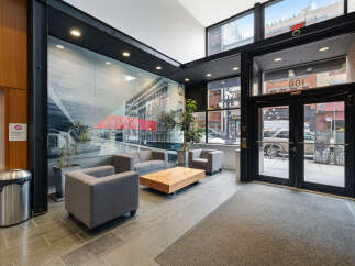 Step into a modern and inviting lobby featuring comfortable grey seating arrangements and a rustic wooden coffee table.