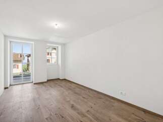 This empty room features a large glass door and a window offering views of the surrounding neighborhood.