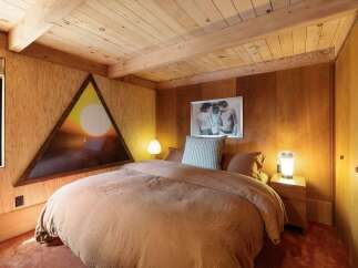 Experience rustic charm in this cozy bedroom, featuring warm wood paneling and a unique triangular window with a sunset view.