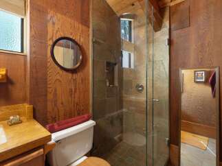 Experience rustic charm in this bathroom featuring warm wood paneling and a spacious glass-enclosed shower with slate tile accents.