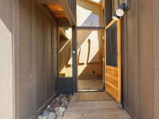 Step into this unique home through a charming wooden door, leading to an interior with striking wood paneling and natural light.