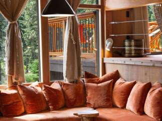 Experience breathtaking mountain views from this stunning living space, featuring a plush, curved sectional sofa adorned with rich terracotta pillows.