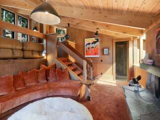 Experience rustic charm in this cozy living room, featuring a striking curved orange velvet sectional sofa and a natural wood staircase.