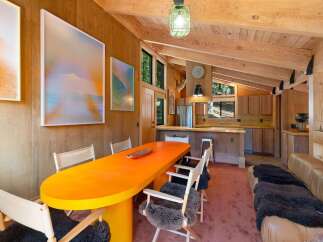 Experience rustic charm and modern comfort in this open-concept living and dining area, featuring a vibrant orange dining table and plush seating.