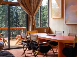 Experience cozy dining with a view in this charming space, featuring a vibrant orange table and comfortable seating.