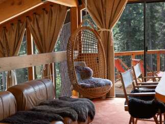 Experience rustic charm and modern comfort in this inviting living space, featuring a cozy leather sofa adorned with plush throws and a unique hanging rattan chair perfect for relaxation.