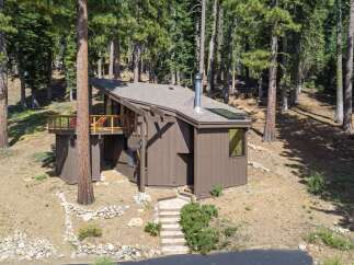 Nestled amidst tall pine trees, this charming home offers a unique A-frame design with a spacious wooden deck perfect for enjoying the serene forest surroundings.