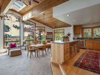 Experience breathtaking views from this stunning home featuring a spacious open-concept living and dining area with a vaulted, wood-paneled ceiling and expansive windows.