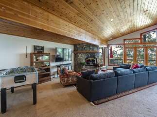 Experience breathtaking mountain views from this stunning living room, featuring a grand stone fireplace and a vaulted wood-paneled ceiling.