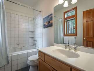 This bathroom features a classic white tiled bathtub and shower combination, complemented by a modern vanity with a white countertop and wooden cabinets.