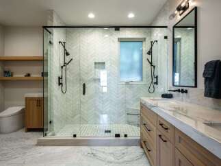 Experience luxury in this modern bathroom featuring a spacious glass-enclosed shower with dual showerheads and elegant herringbone tilework.