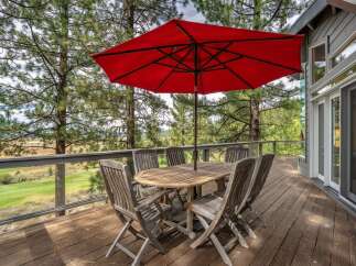 Enjoy outdoor dining and relaxation on this spacious wooden deck, complete with a large red umbrella and a rustic wooden table set.